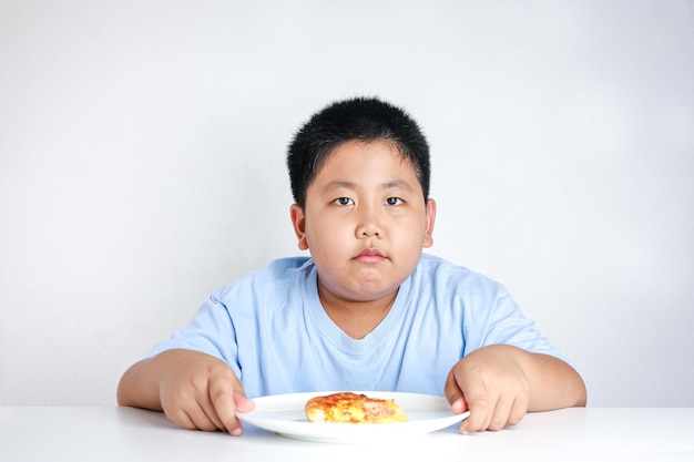 Gruby chłopiec trzymał talerz do pizzy spoczywający na białym stole.