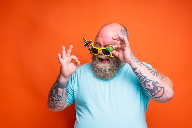 Gruby szczęśliwy mężczyzna z tatuażami na brodzie i okularami przeciwsłonecznymi jest gotowy na lato