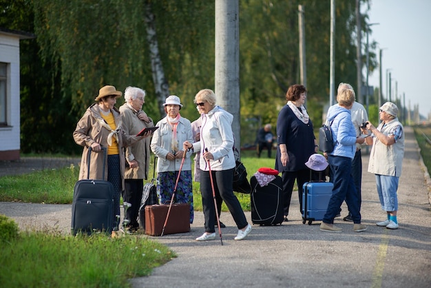 Grupa aktywnych wesołych seniorów stojących na peronie z walizkami