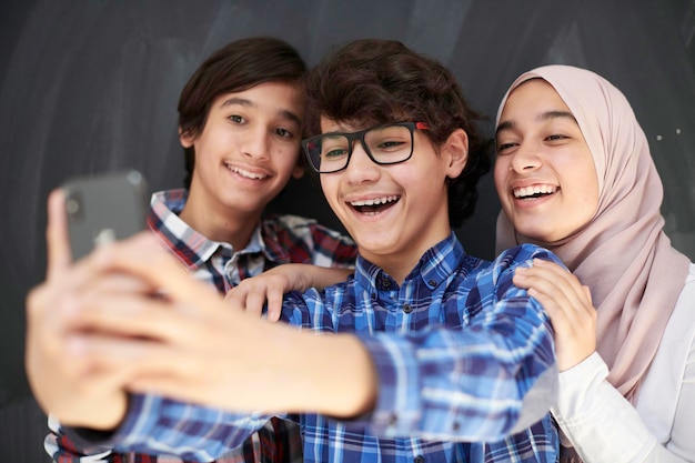 grupa arabskich nastolatków robi zdjęcie selfie na smartfonie z czarną tablicą w tle