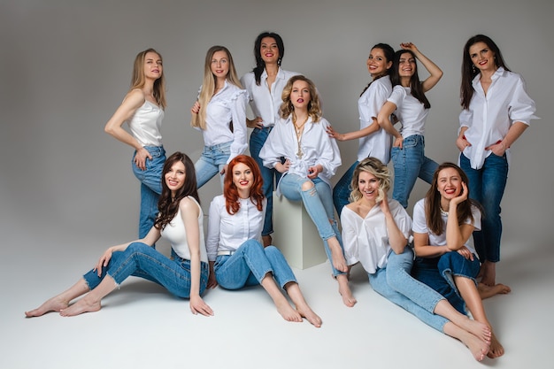 Grupa atrakcyjnych młodych dorosłych kobiet na sobie niebieskie dżinsy i biały top, uśmiechając się z przodu pozowanie