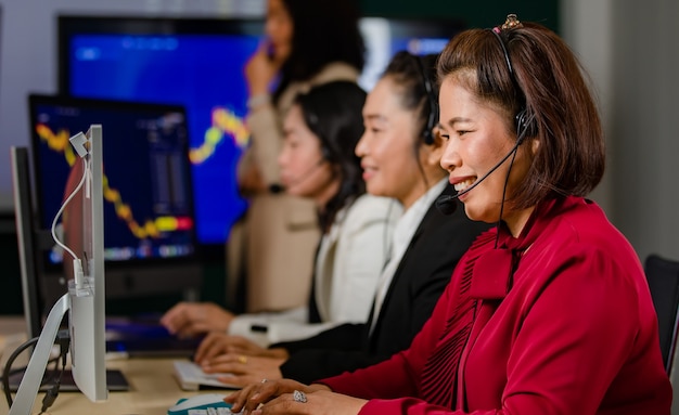 Grupa azjatyckich operatorów obsługi klienta nosi słuchawki z mikrofonem, uśmiechając się z przodu, codzienny wykres