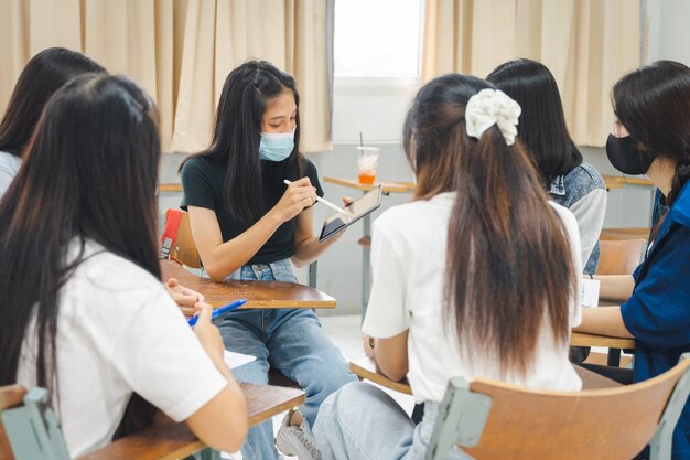 Grupa azjatyckich studentów uniwersyteckich nosi maskę ochronną na twarz omawia projekt w klasie