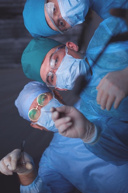 Grupa chirurgów w pracy na sali operacyjnej stonowanych na niebiesko Zespół medyczny wykonujący operację
