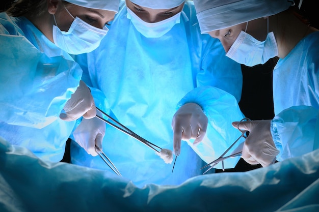 Zdjęcie grupa chirurgów w pracy na sali operacyjnej w odcieniach niebieskiego. zespół medyczny wykonujący operację