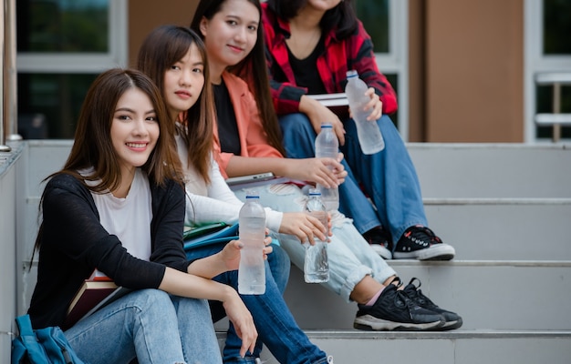 Grupa Czterech Atrakcyjnych Azjatyckich Studentów Siadających Na Każdej Klatce Schodowej W Odkrytym Kampusie Uniwersyteckim. Koncepcja Edukacji, Przyjaźni I życia Studentów.