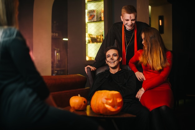 Zdjęcie grupa czterech przyjaciół świętuje halloween w kawiarni. faceci przebrani za przerażające świąteczne potwory. rzeźbiona dynia na stole.