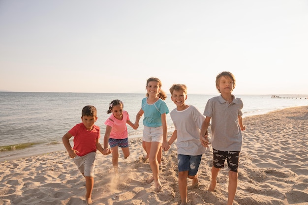 Grupa dzieci bawiących się na plaży biegające i uśmiechnięte Dzieci korzystające z letnich wakacji