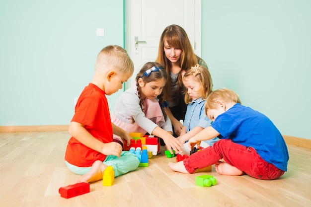 Grupa dzieci bawiących się zabawkami konstrukcyjnymi klocki budowanie wieży w pokoju. Matka bawi się z dziećmi, floortime.