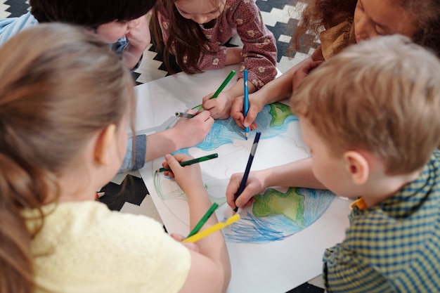 Grupa dzieci siedzących przy stole i wspólnie rysujących obrazek kredkami