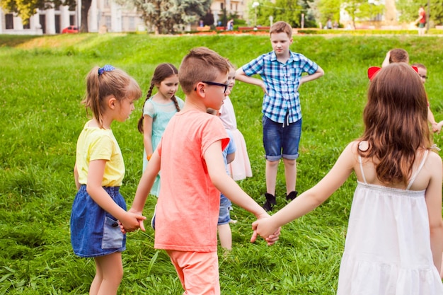 Grupa dzieci trzymających się za ręce i tańczących w kręgu na zielonym trawniku w piękny letni dzień