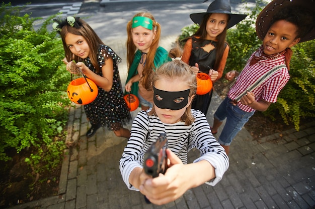 Grupa dzieci w kostiumach na Halloween grających cukierek albo psikus podczas wakacji stojących na zewnątrz i uśmiechając się do kamery