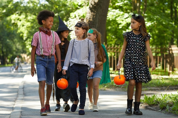 Grupa dzieci w kostiumach z zabawkowymi dyniami spacerującymi ulicą, aby uczcić święto Halloween