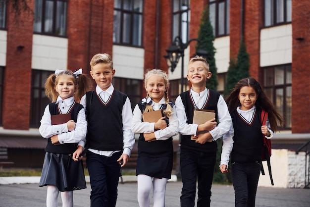 Grupa Dzieci W Mundurkach Szkolnych, Która Jest Razem Na Zewnątrz W Pobliżu Budynku Edukacji.