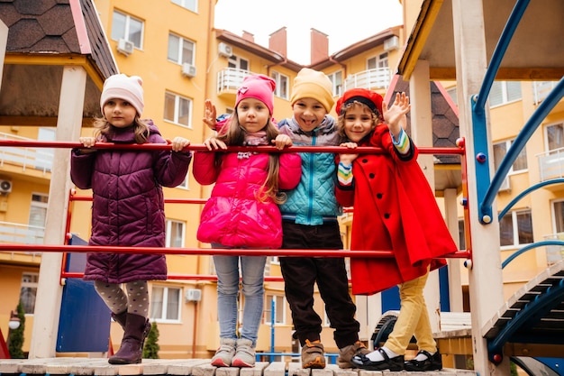 Grupa dzieciaków spacerujących po placu zabaw w zimną pogodę Dzieci ubrane w kurtki i czapki na wiosnę