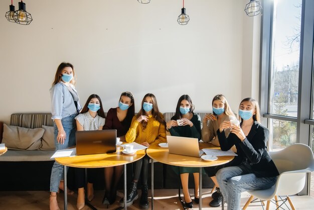 Grupa Dziewcząt W Maskach Siedzi W Kawiarni I Pracuje Na Laptopach. Nauczanie Studentów.