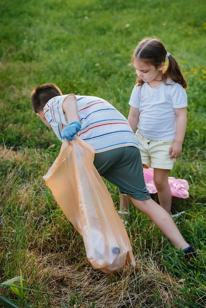 Grupa dziewczyn z dziećmi o zachodzie słońca zajmuje się wywozem śmieci w parku. Troska o środowisko, recykling.