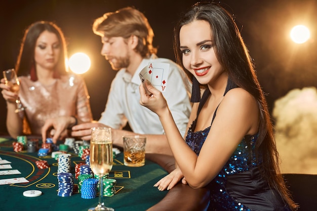 Grupa Eleganckich Ludzi Grających W Pokera W Kasynie. Skup Się Na Luksusowej Brunetce W Niebieskiej Błyszczącej Sukience