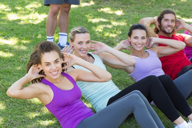 Zdjęcie grupa fitness robi siedzieć ups w parku z trenerem