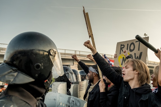 Grupa funkcjonariuszy policji w hełmach trzymających tarcze podczas zamieszek podczas atakowania rebeliantów za pomocą znaków na zewnątrz