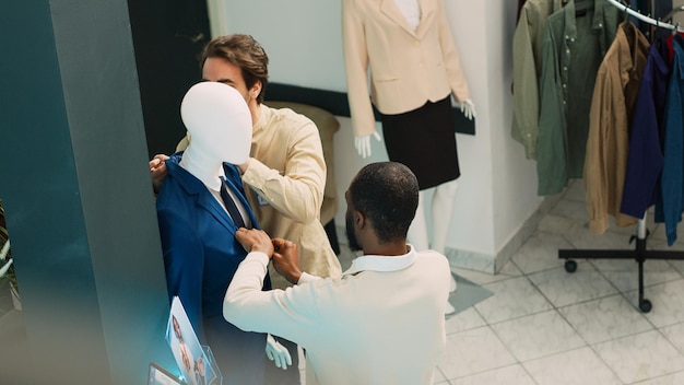 Grupa klientów oglądających nową kolekcję mody w sklepie odzieżowym, różnorodni ludzie sprawdzający towary butikowe w centrum handlowym. Mężczyźni i kobiety odwiedzający sklep detaliczny. Strzał z ręki.