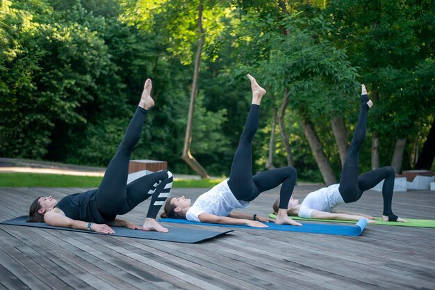 Grupa kobiet ćwiczy jogę leżąc na macie do jogi Ćwiczenie z podniesioną nogą Fitness w parku