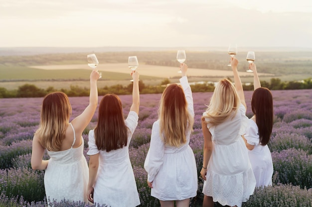 Grupa kobiet w białych sukienkach trzyma kieliszki wina na lawendowym polu