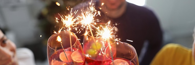 Grupa ludzi pijących koktajle ze szklanek z zimnymi ogniami przed zbliżeniem choinki