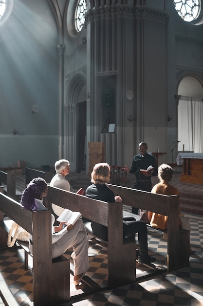 Grupa ludzi siedząca na ławce i słuchająca przemówienia księdza podczas mszy