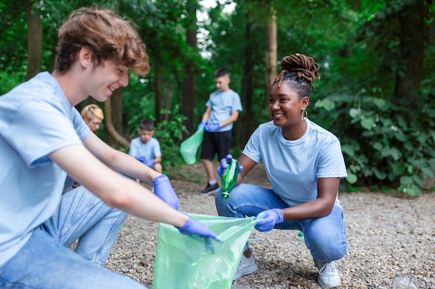Grupa ludzi sprząta razem w publicznym parku chroniąc środowisko Kobieta na pierwszym planie z workiem na śmieci w dłoni sprząta park