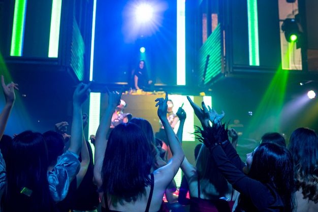 Grupa ludzi tańczy w dyskotece w rytm muzyki DJ-a na scenie