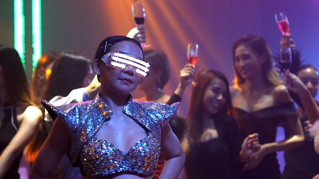 Grupa ludzi tańczy w nocnym klubie disco w rytm muzyki DJ-a na scenie
