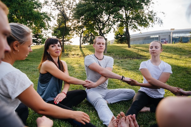 Grupa ludzi uprawia jogę w kręgu na świeżym powietrzu podczas zachodu słońca. Zdrowy styl życia, medytacja i dobre samopoczucie.
