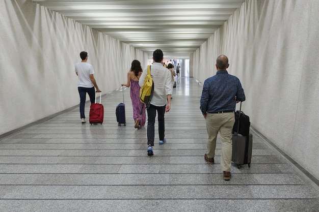 Grupa ludzi z walizkami na kółkach przechodzi przez widok z tyłu przejścia podziemnego