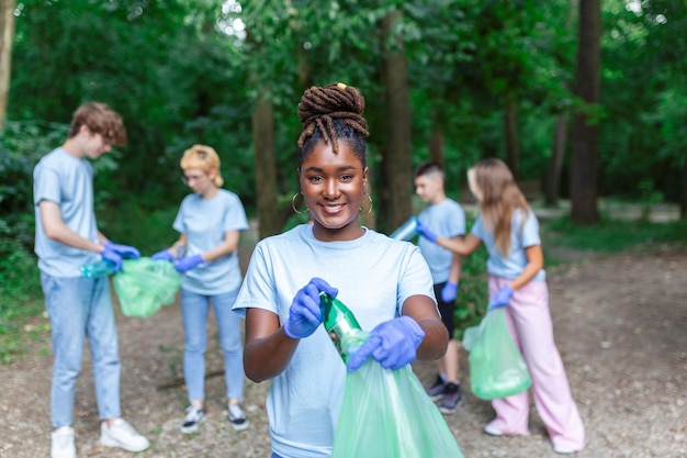 Grupa młodych ludzi przyjaciół wolontariuszy zbierających plastikowe butelki do worków na śmieci w lesie Koncepcja ekologii