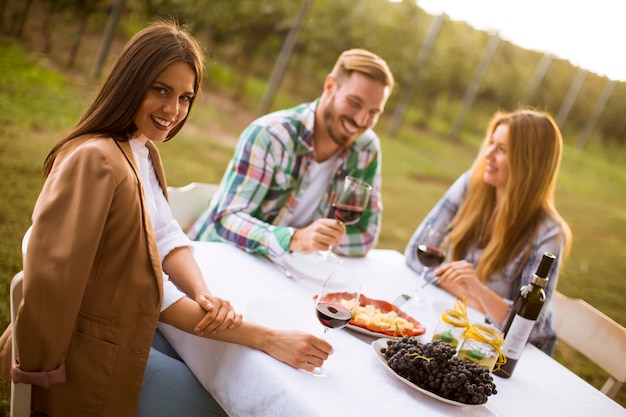 Grupa młodych ludzi siedzi przy stole i pije czerwone wino w winnicy