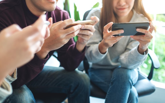 Grupa młodych ludzi używających i grających w gry na telefonie komórkowym, siedząc razem