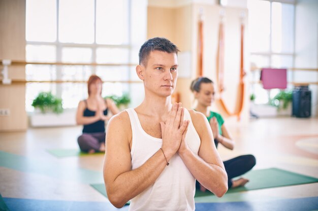 Grupa Młodych Sportowców ćwiczących Lekcję Jogi Z Instruktorem, Siedząca W ćwiczeniu Padmasana, Pozy Lotus Z Założonymi Rękami W Namaste