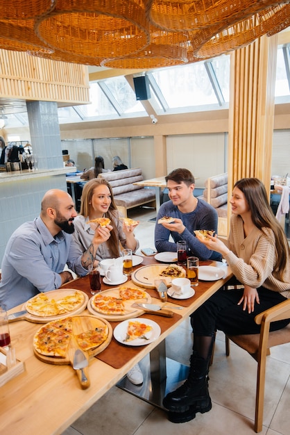 Grupa Młodych Wesołych Przyjaciół Siedzi W Kawiarni Rozmawiając I Jedząc Pizzę. Obiad W Pizzerii.