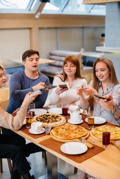 Grupa Młodych Wesołych Przyjaciół Siedzi W Kawiarni Rozmawiając I Robiąc Sobie Selfie Przez Telefon