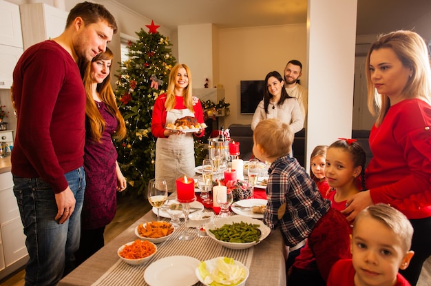 Grupa najlepszych przyjaciół zebrała się razem na świąteczny obiad. Młodzi rodzice i ich dzieci przy stole pełnym pysznego jedzenia, gospodyni trzymająca talerz z daniem głównym