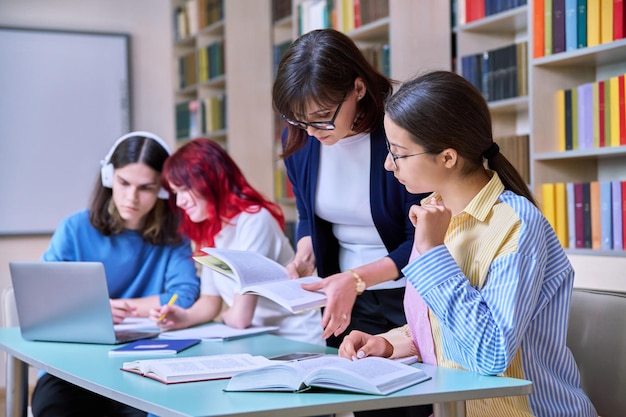 Grupa nastoletnich uczniów studiuje w klasie biblioteki szkolnej Nastoletnia dziewczyna i mentorka nauczycielki pomagają w nauce Uczenie się w szkole średniej Edukacja Wiedza Dorastanie