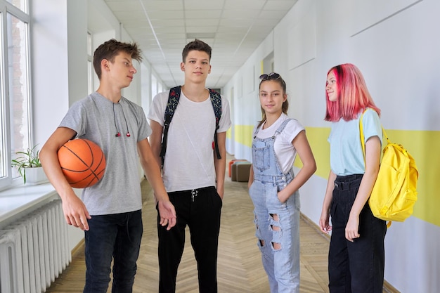 Grupa nastoletnich uczniów w wieku 16 lat na korytarzu szkolnym Spacerujący rozmawiający nastolatki z piłką do koszykówki z plecakami