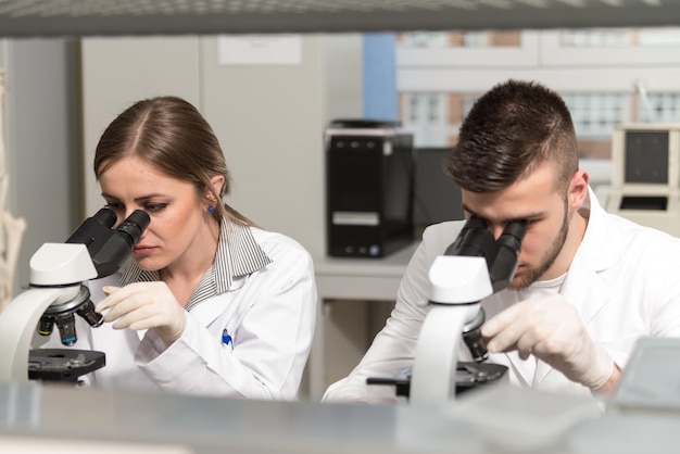 Grupa naukowców prowadzących badania w środowisku laboratoryjnym patrząca w mikroskop