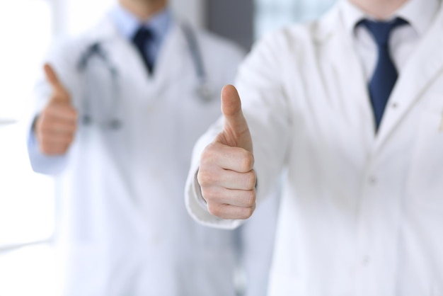 Grupa nowoczesnych lekarzy stojących jako zespół z kciukami do góry lub znakami OK w zbliżeniu biura szpitala