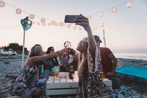 Grupa przyjaciele robi przyjęciu na plaży przy zmierzchu czasem