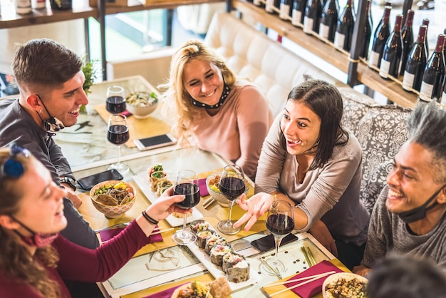 Grupa przyjaciół cieszących się posiłkiem w restauracji, ochrona maski covid19, młodzi ludzie wznoszący tosty z czerwonym winem i dobrze się bawiący, koncentrują się na brunetce