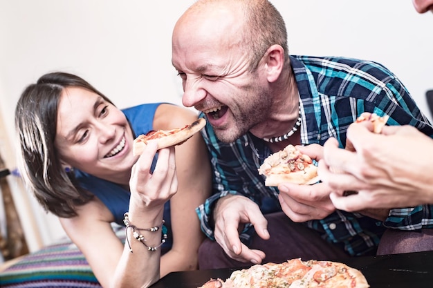 Grupa przyjaciół je i bawi się Uśmiechnięta kobieta próbuje nakarmić mężczyznę swoim kawałkiem pizzy