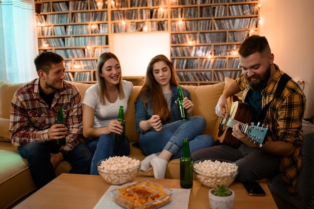 Zdjęcie grupa przyjaciół na imprezie domowej grająca na gitarze i pijąca piwo