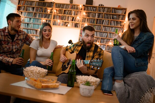 Grupa przyjaciół na imprezie w domu gra na gitarze i dobrze się bawi